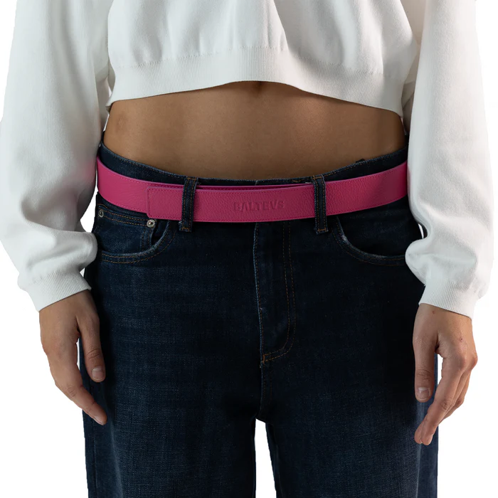 En la foto aparece la cadera de una persona que lleva un cinturon balteus de cuero rosa con cierre de velcro sujetando unos jeans azules y una camiseta blanca.