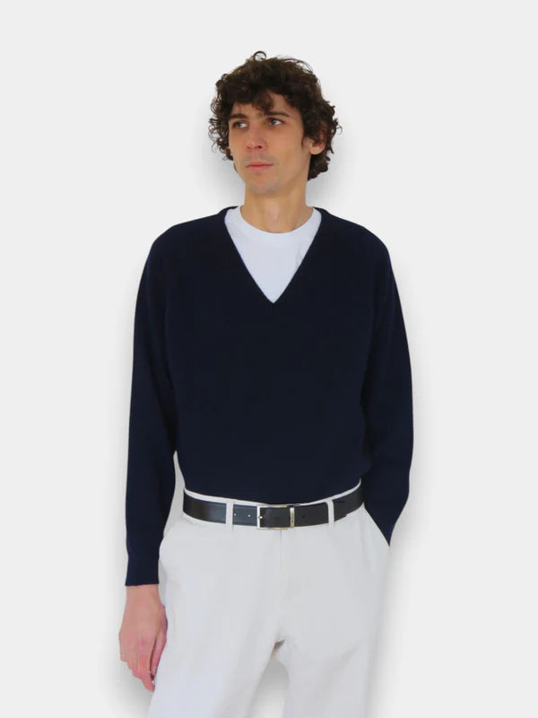 En la foto aparece una chico que lleva un cinturon de color negro con hebilla metálica reversible, sujetando un pantalon blanco y un jersey azul.