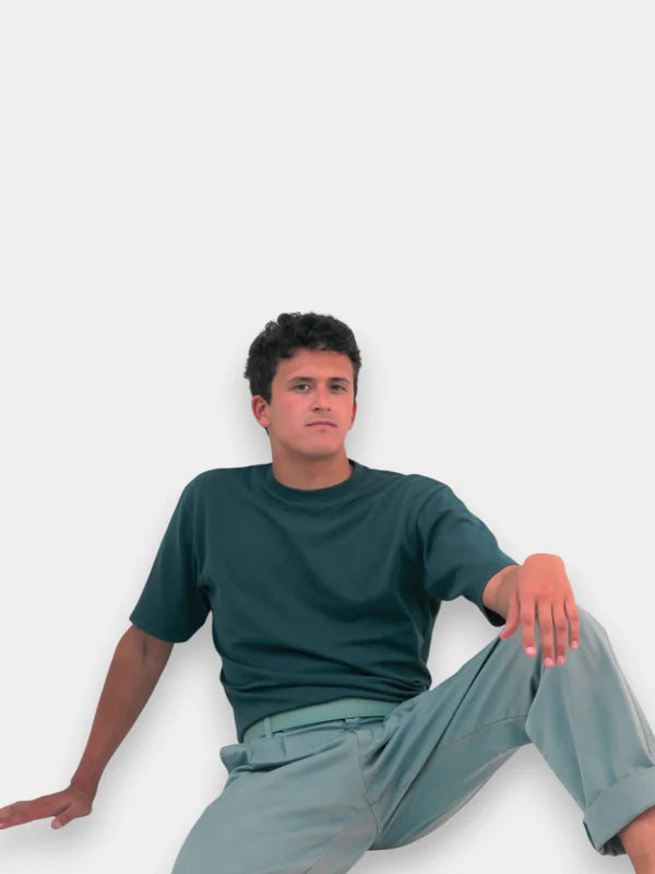 En la foto aparece un chico que lleva un cinturon de cuero verde kiwi y cierre de velcro, sujetando unos pantalones grises y una camiseta verde.