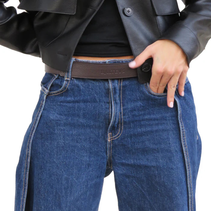 En la foto aparece la cadera de una persona que lleva un cinturon balteus de cuero marron chocolate con cierre de velcro sujetando unos jeans azules, una camiseta negra y una chaqueta de cuero negra.