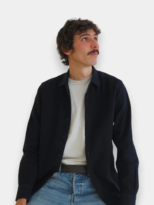 En la foto aparece un chico que lleva un cinturon balteus de cuero marron chocolate y con cierre de velcro, sujetando unos jeans azules, una camiseta blanca y una camisa azul.